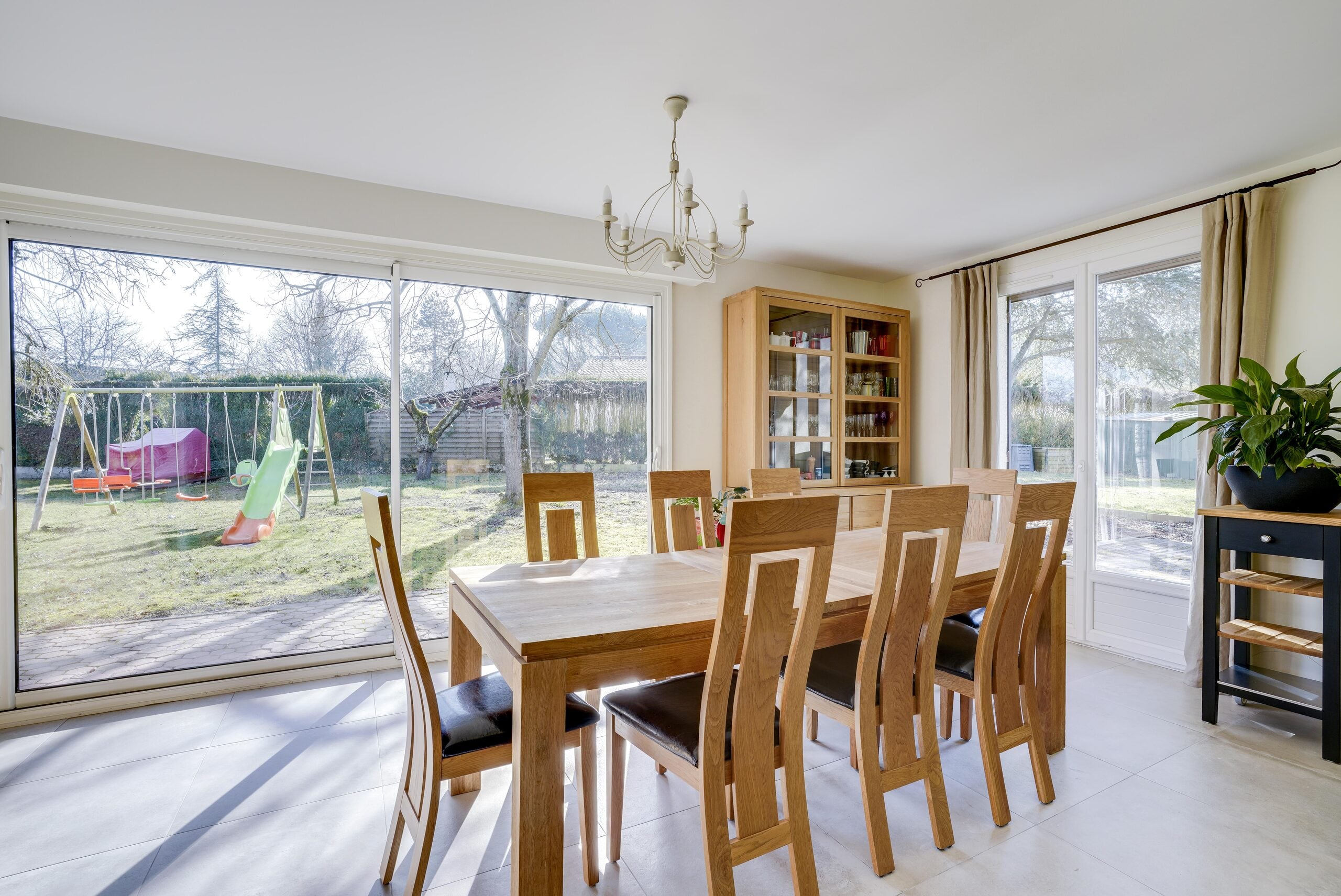 Salle à manger lumineuse en chêne avec grande baie vitrée ouvrant sur un jardin avec balançoire — réalisation Dec Home