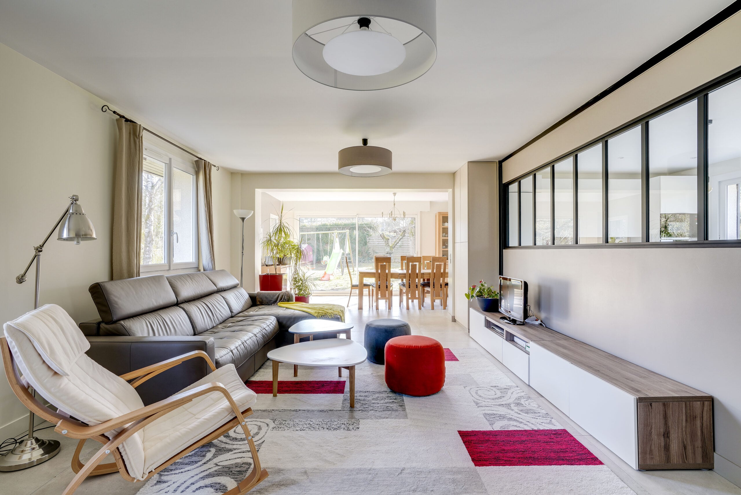 Salon contemporain avec canapé d'angle en cuir anthracite, verrière noire et vue sur la salle à manger — réalisation Dec Home