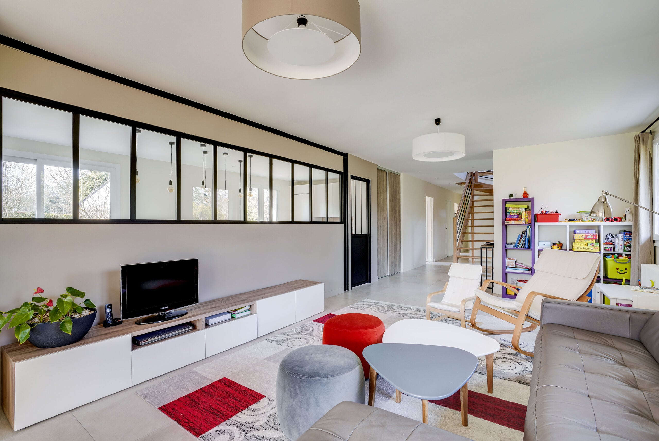 Salon moderne avec verrière industrielle noire, meuble TV bas blanc et coin salon familial — réalisation Dec Home