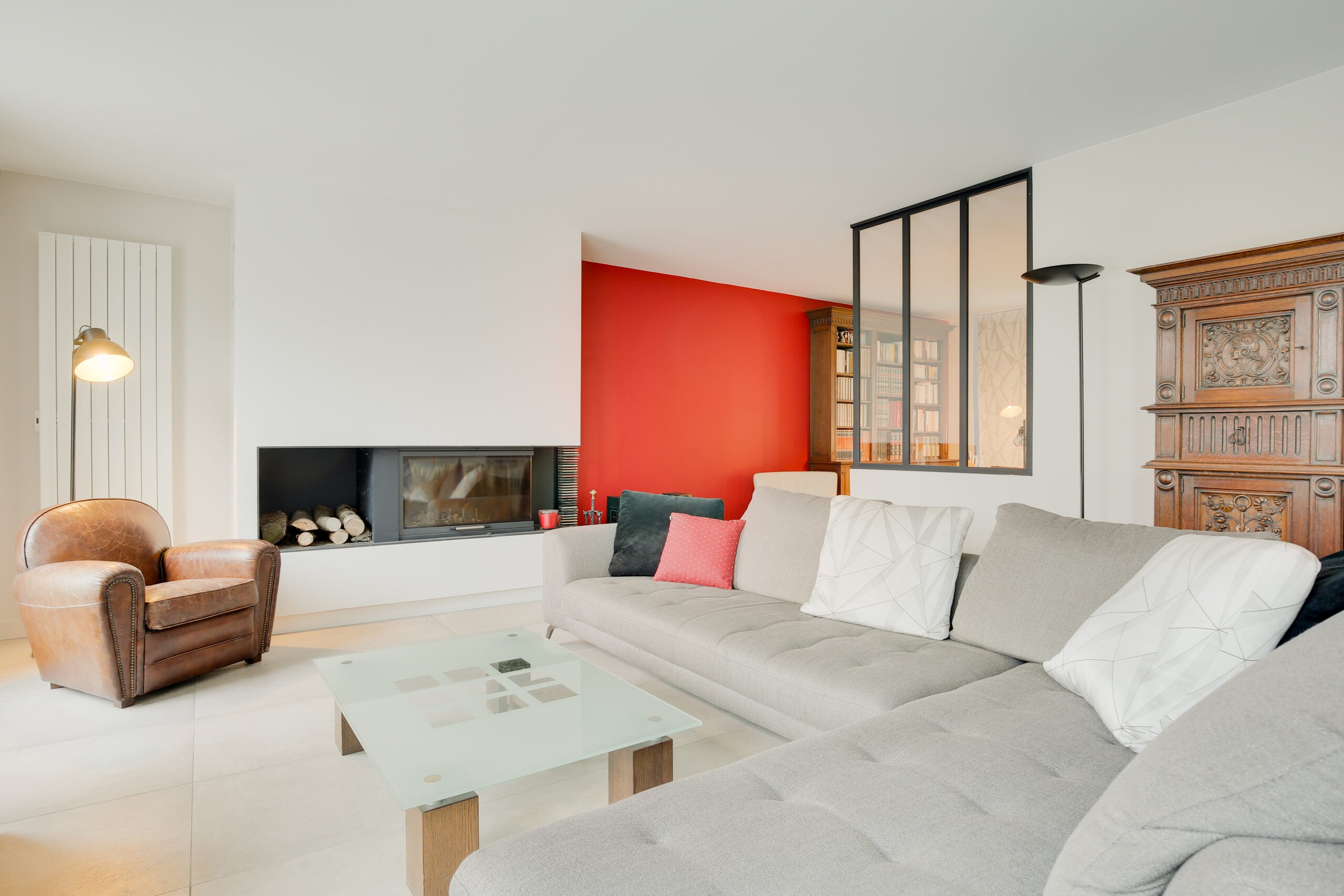 Salon avec cheminée insert contemporaine, mur d'accent rouge, canapé gris et fauteuil club en cuir — réalisation Dec Home