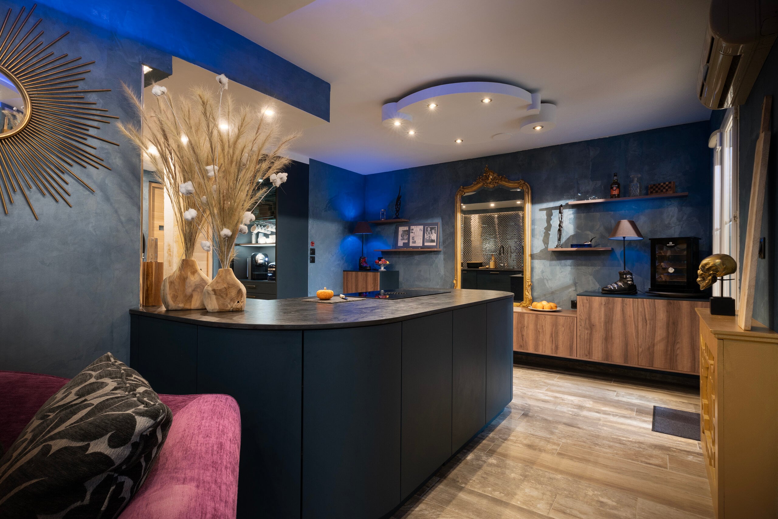 Cuisine sur-mesure avec armoires en bois bleu foncé, îlot courbe et canapé violet en arrière-plan