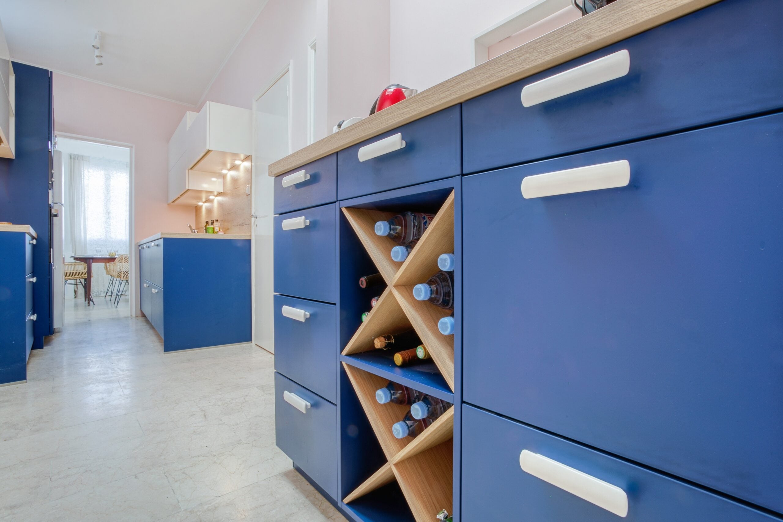 Détail des rangements bleus avec casier à bouteilles en bois et poignées blanches