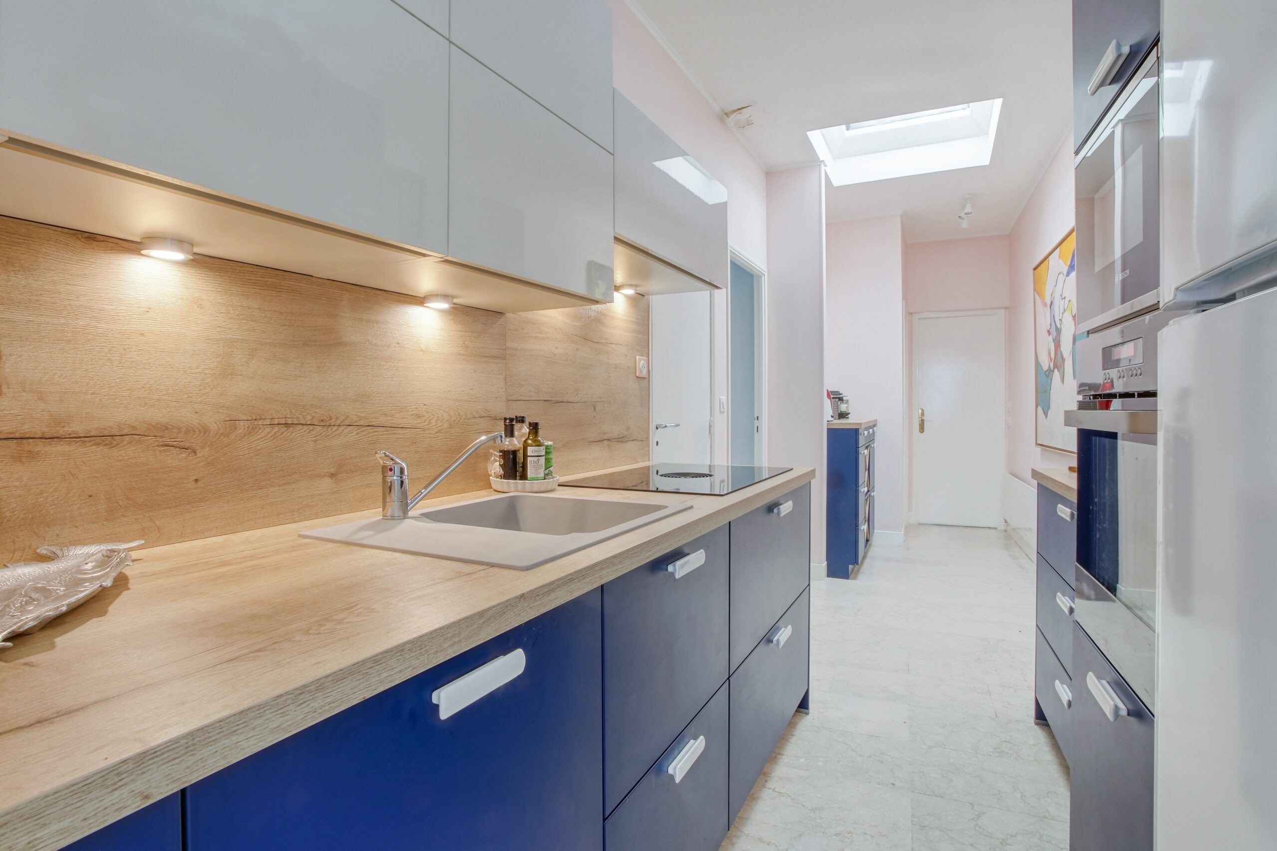 Cuisine longue en galerie avec armoires bleues et comptoir en bois, plaques à induction