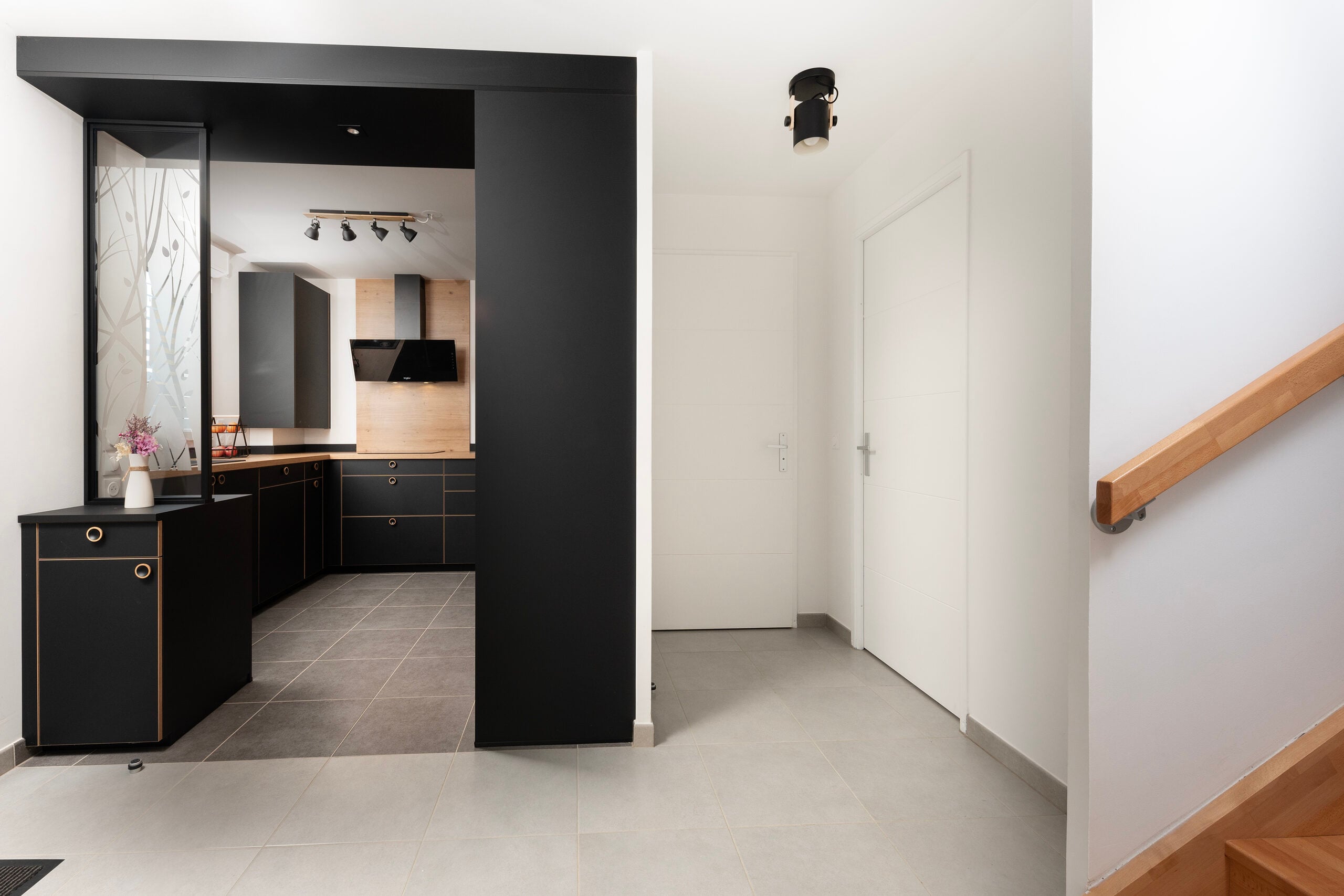 Vue depuis l'entrée sur la cuisine noire avec hotte et plan de travail en bois