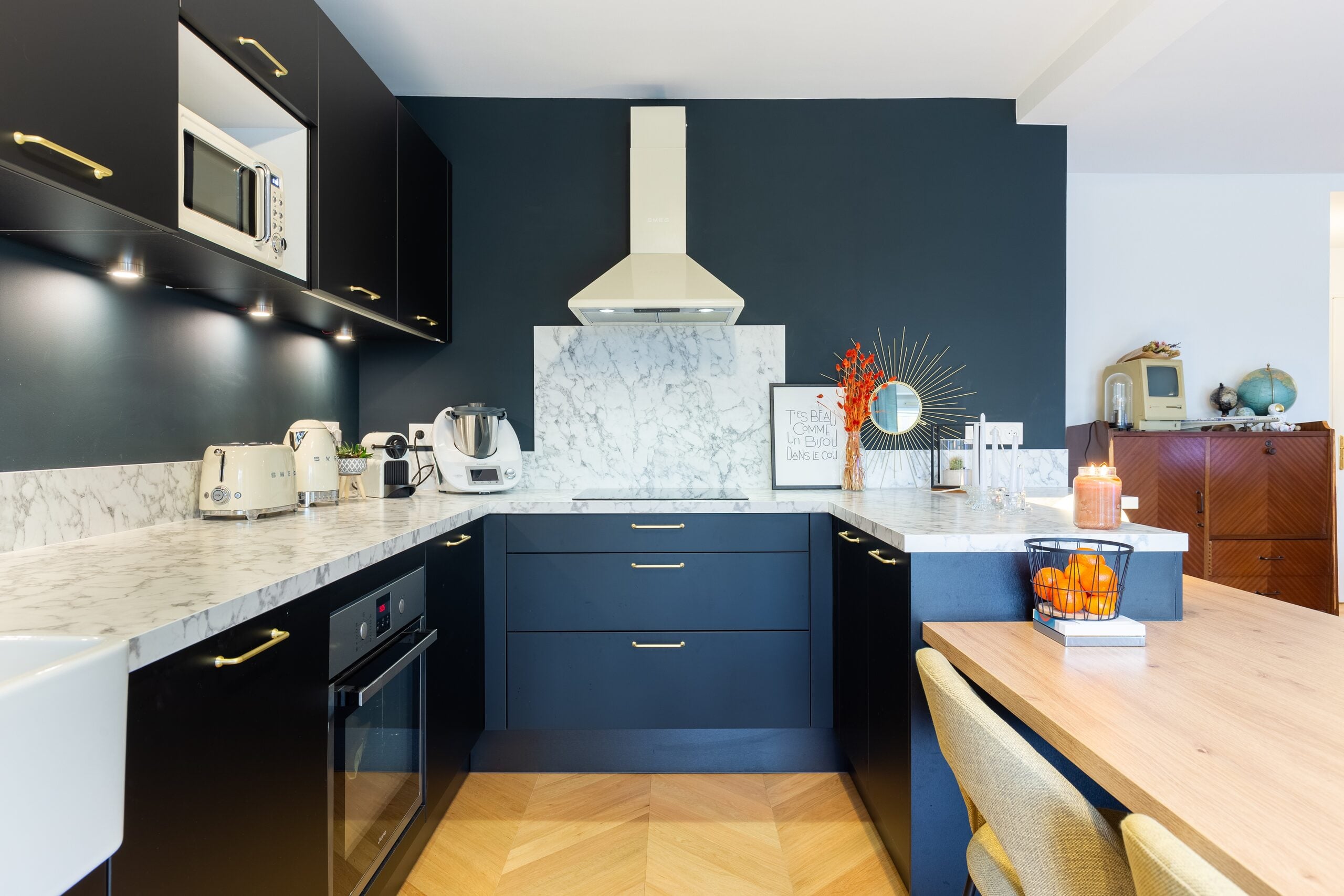 Cuisine aux armoires sombres avec comptoirs en marbre et appareils encastrés