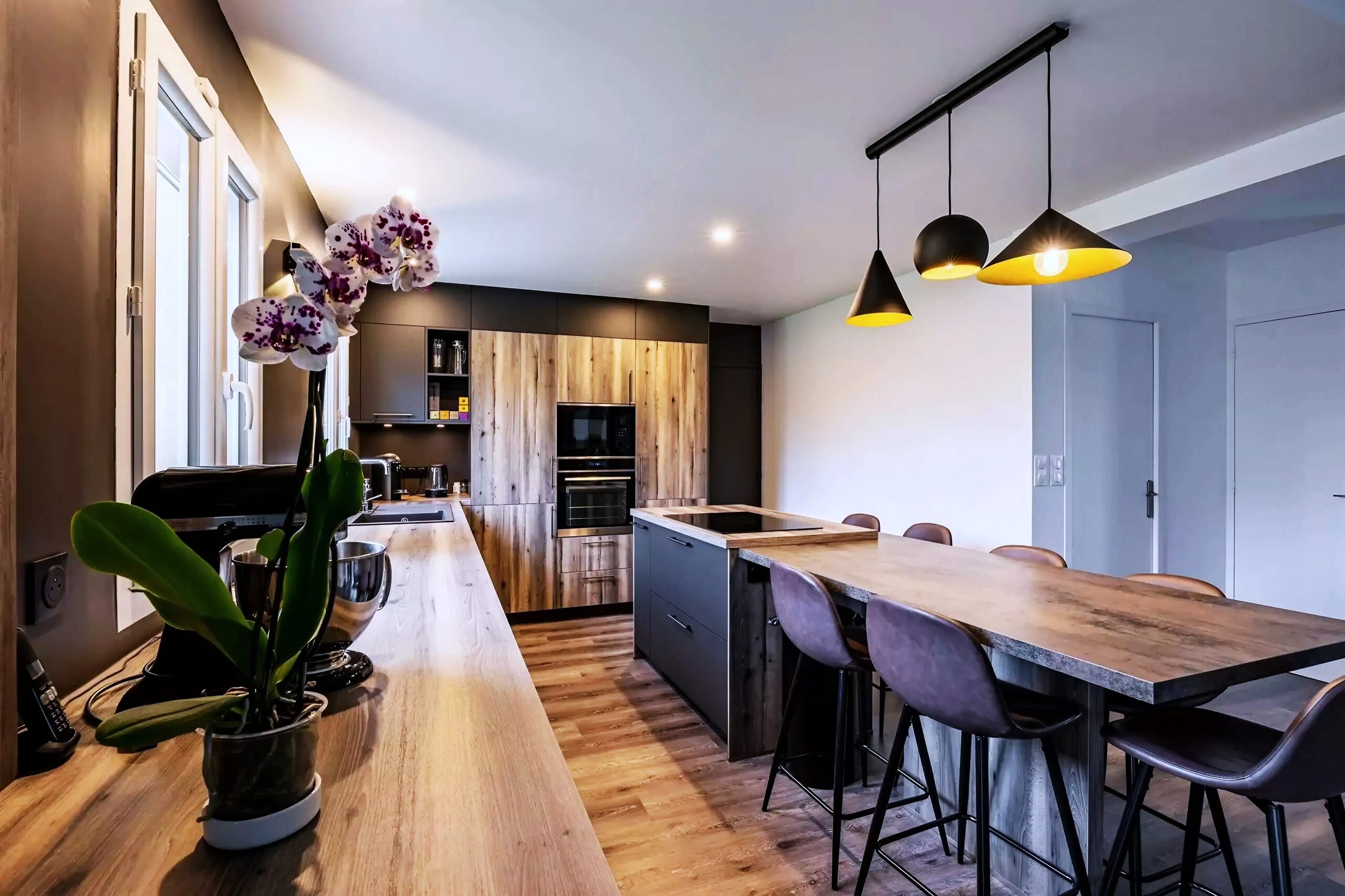 Cuisine nordique avec comptoirs en bois, îlot central, tabourets et fours encastrés — réalisation Dec Home